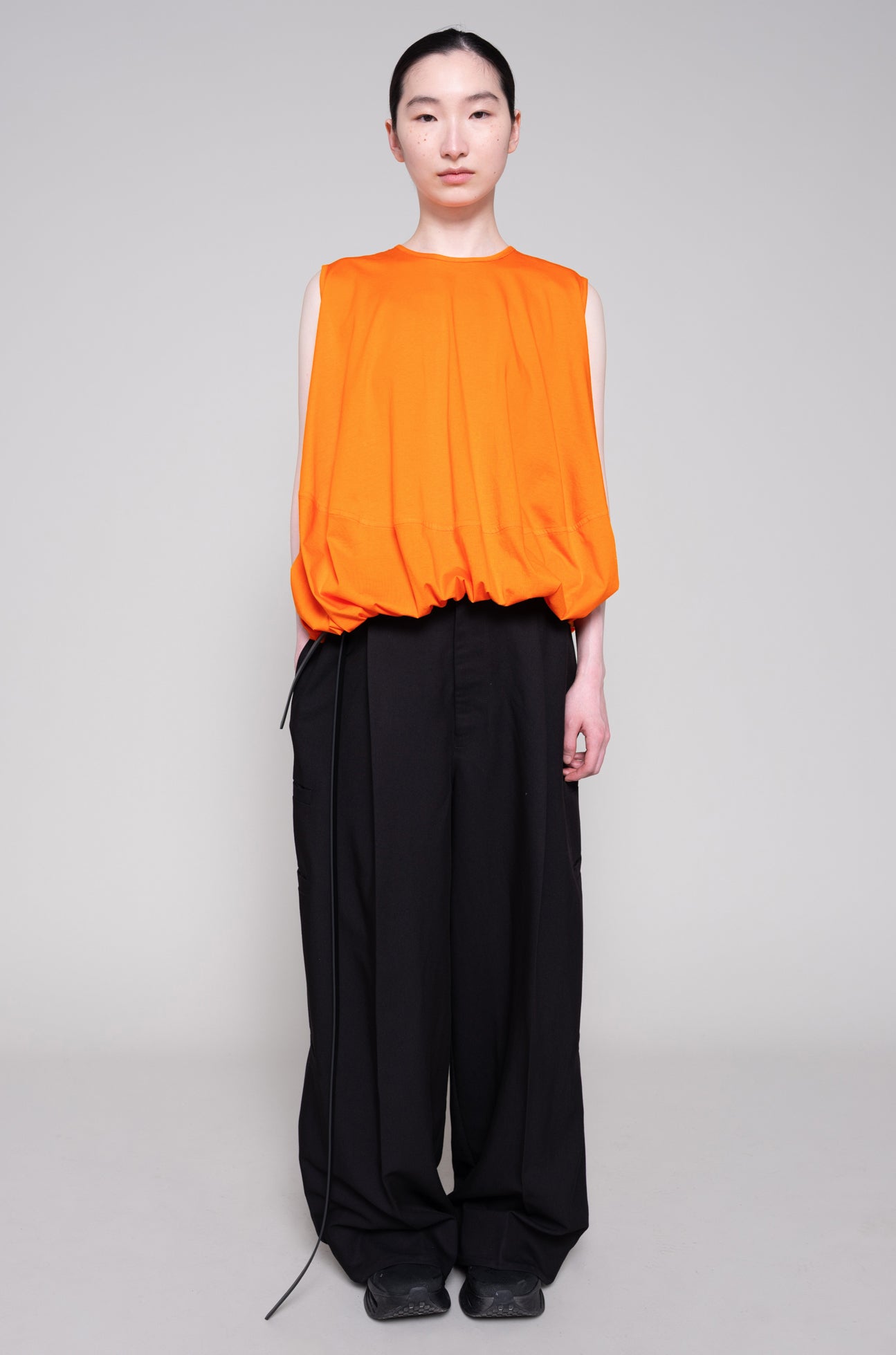 Person wearing an orange sleeveless top and black pants on a plain background