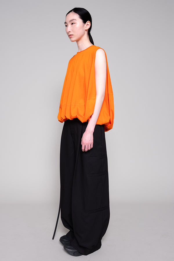 Person wearing an orange sleeveless top and black pants on a gray background