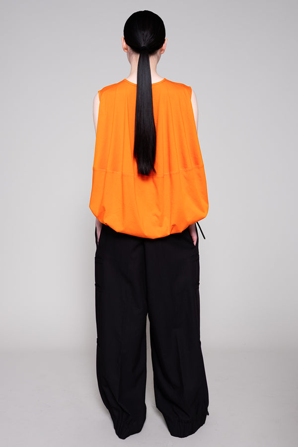 Person wearing an orange sleeveless top and black pants on a gray background