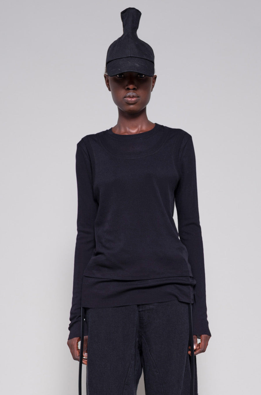 Person wearing a black long sleeve and pants with a hat on a plain background