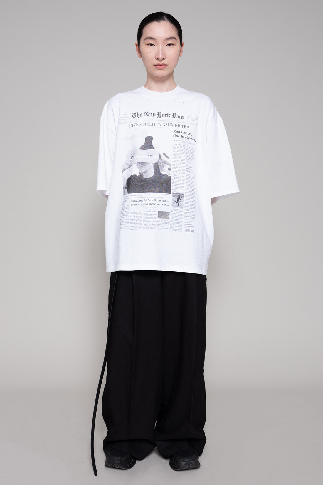 Person wearing a white t-shirt with black text and graphics, paired with black pants on a gray background