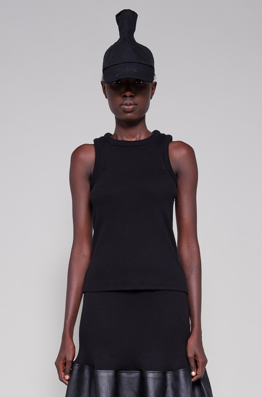 Person wearing a black sleeveless top and black leather skirt with a cap on a plain background