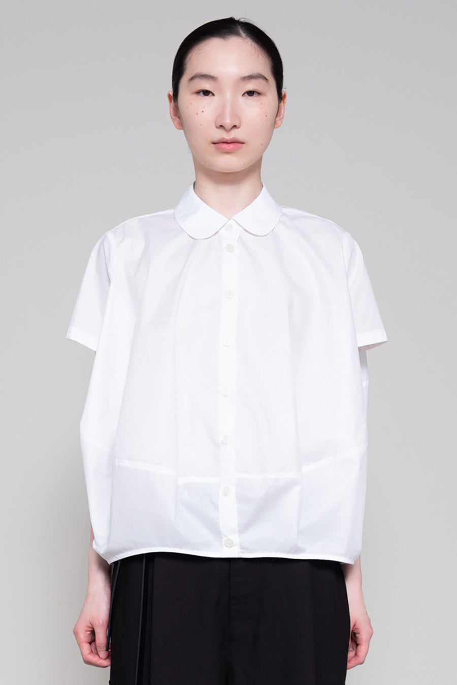 Person wearing a white shirt and black pants on a gray background