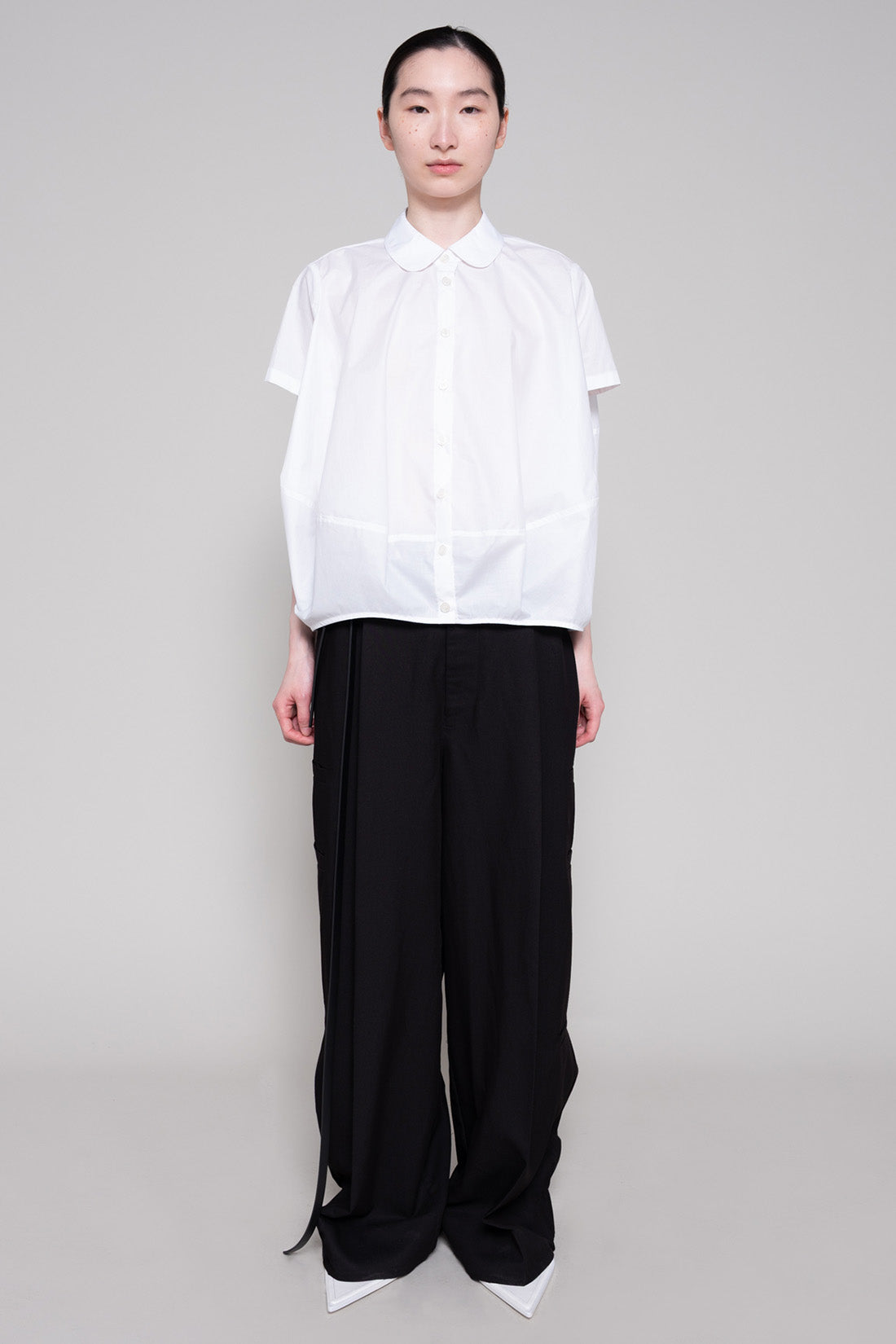 Person wearing a white shirt and black pants on a gray background