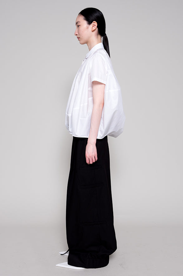 Person wearing a white shirt and black pants on a plain background