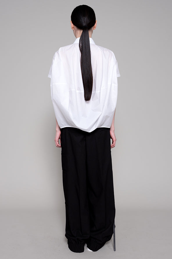 Person wearing a white top and black pants with a plain background