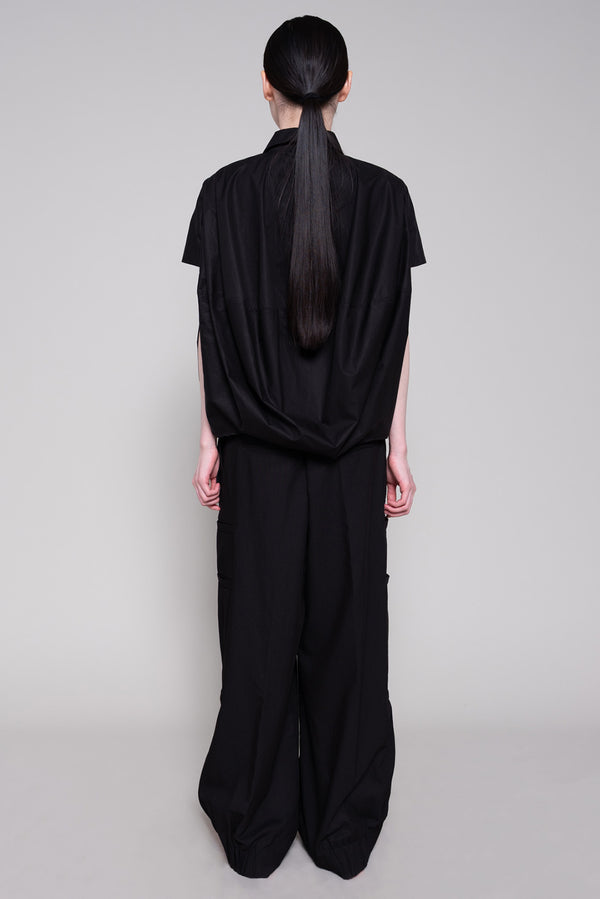 Person wearing a black shirt and pants against a plain background