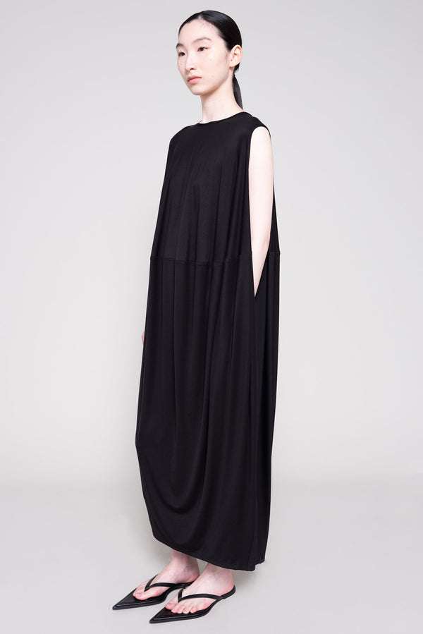 Person wearing a long black dress and flip flops with a plain background