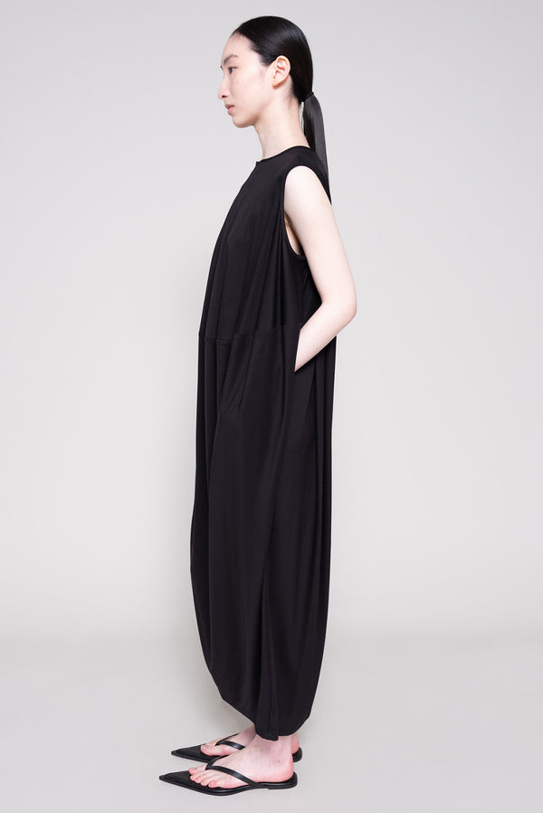 Person wearing a long black dress and flip flops with a plain background
