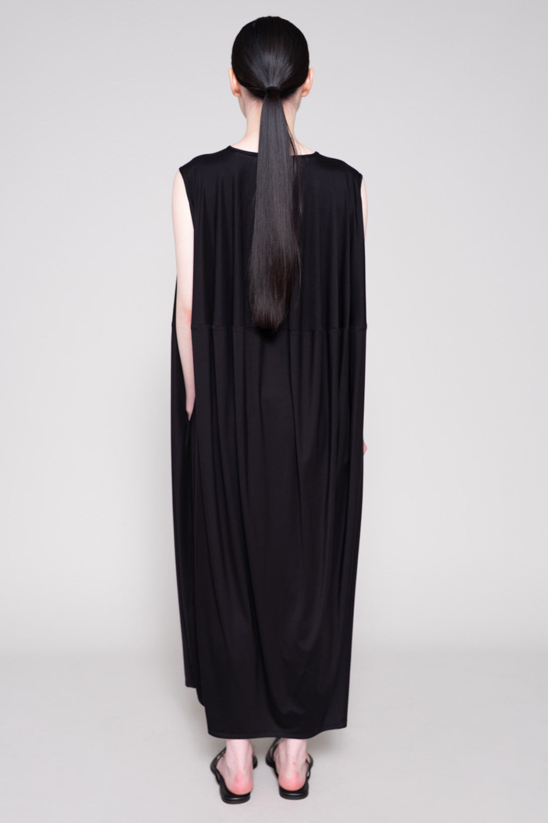 Person wearing a long black dress with a plain background