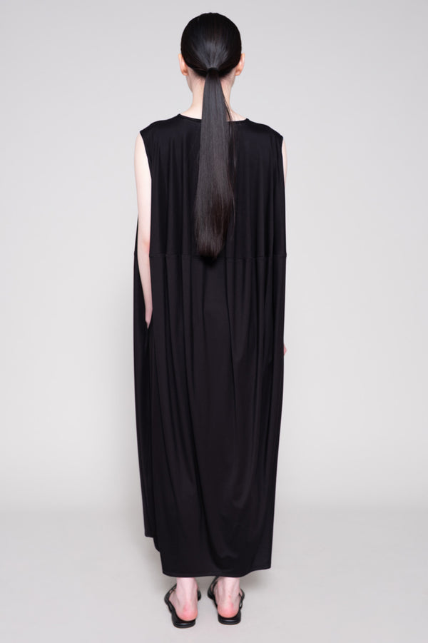 Person wearing a long black dress with a plain background