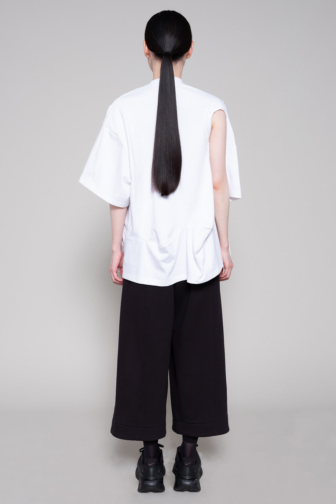 Person wearing a white oversized shirt with cut-out details and black pants on a plain background
