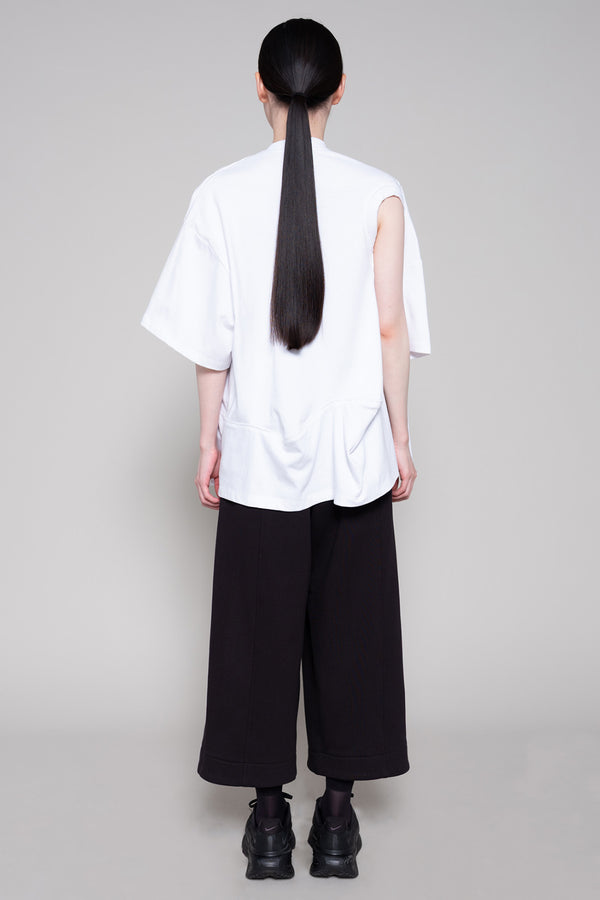 Person wearing a white oversized shirt with cut-out details and black pants on a plain background