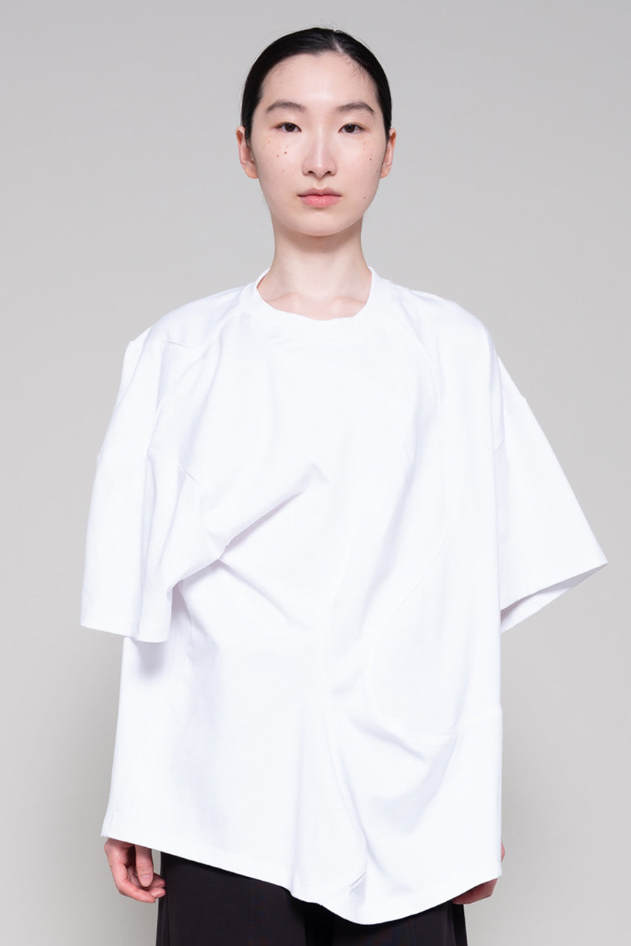 Person wearing a white oversized shirt and black pants on a plain background