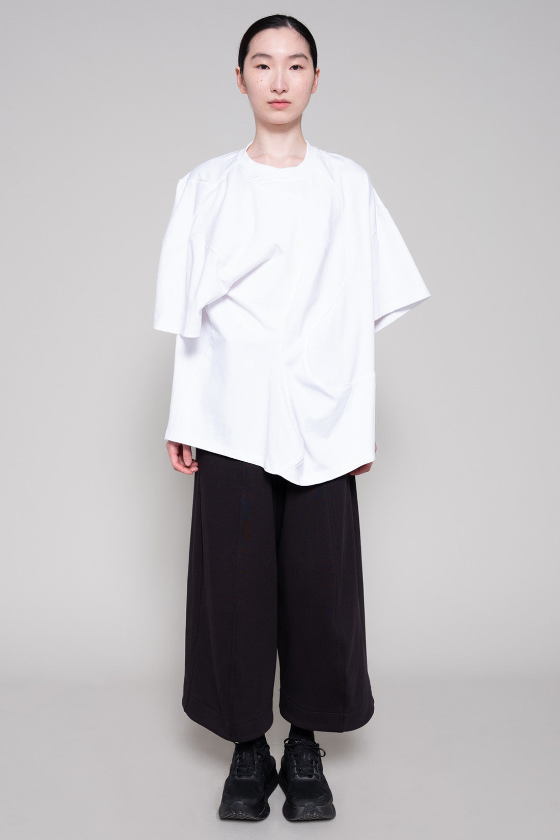 Person wearing a white oversized shirt and black pants on a plain background