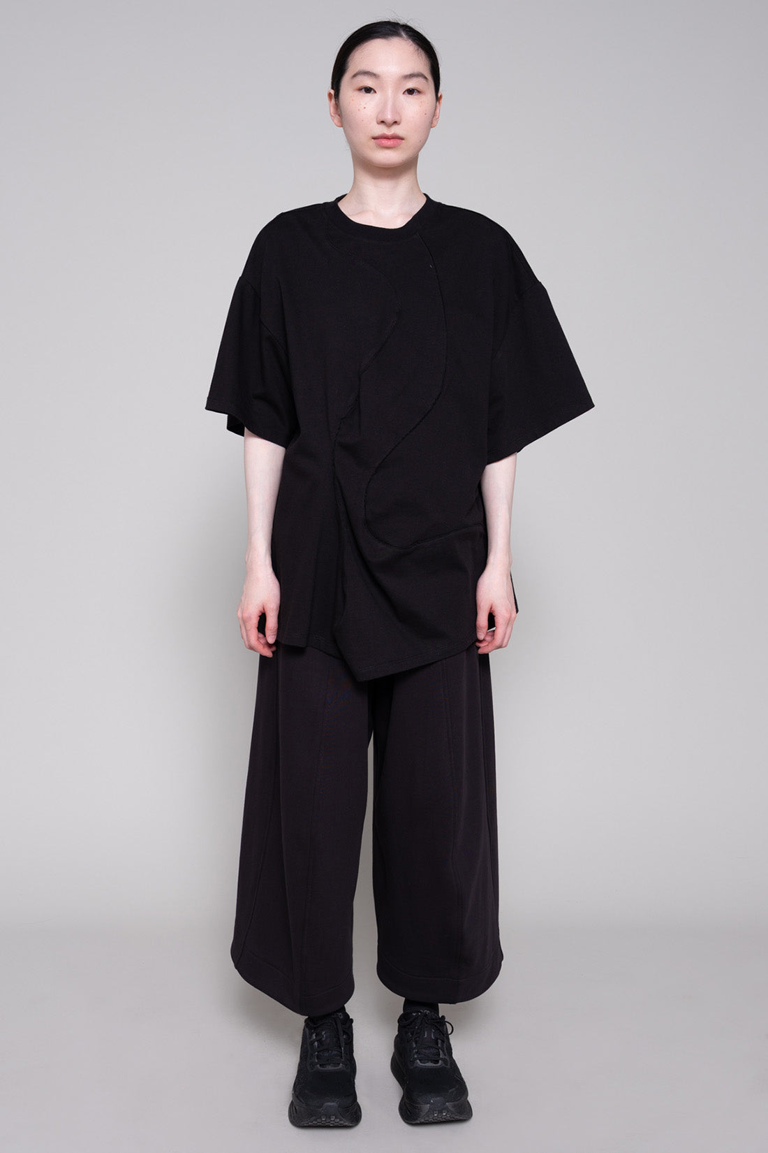 Person wearing a black tee and pants against plain background