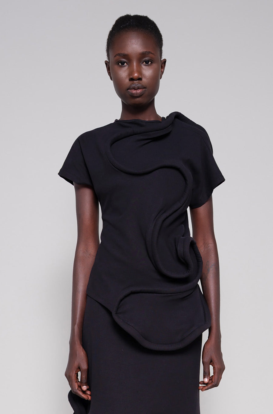 Person wearing a black top and skirt with swirl details against a plain background