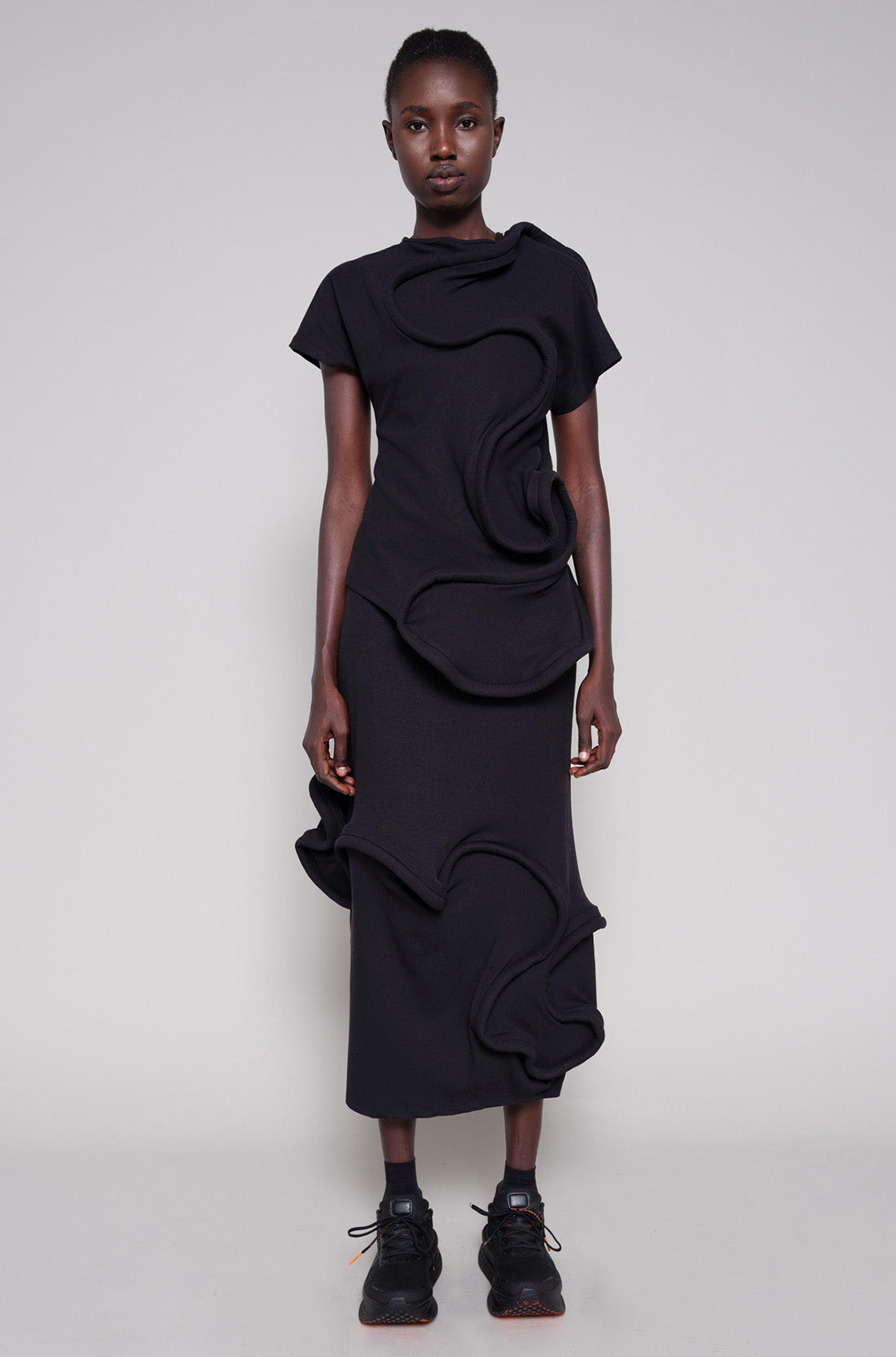 Person wearing a black top and skirt with swirl details against a plain background