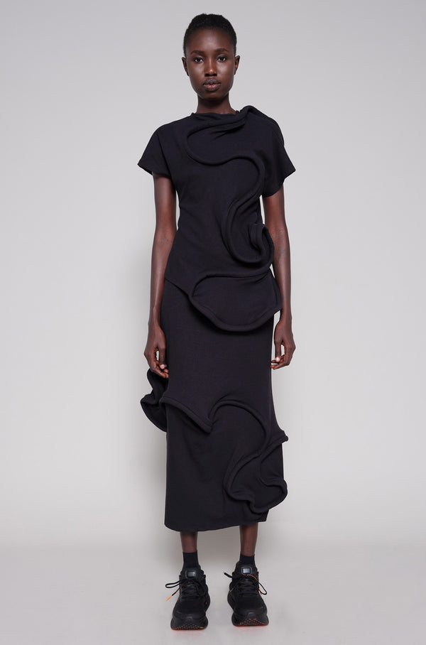 Person wearing a black top and skirt with swirl details against a plain background