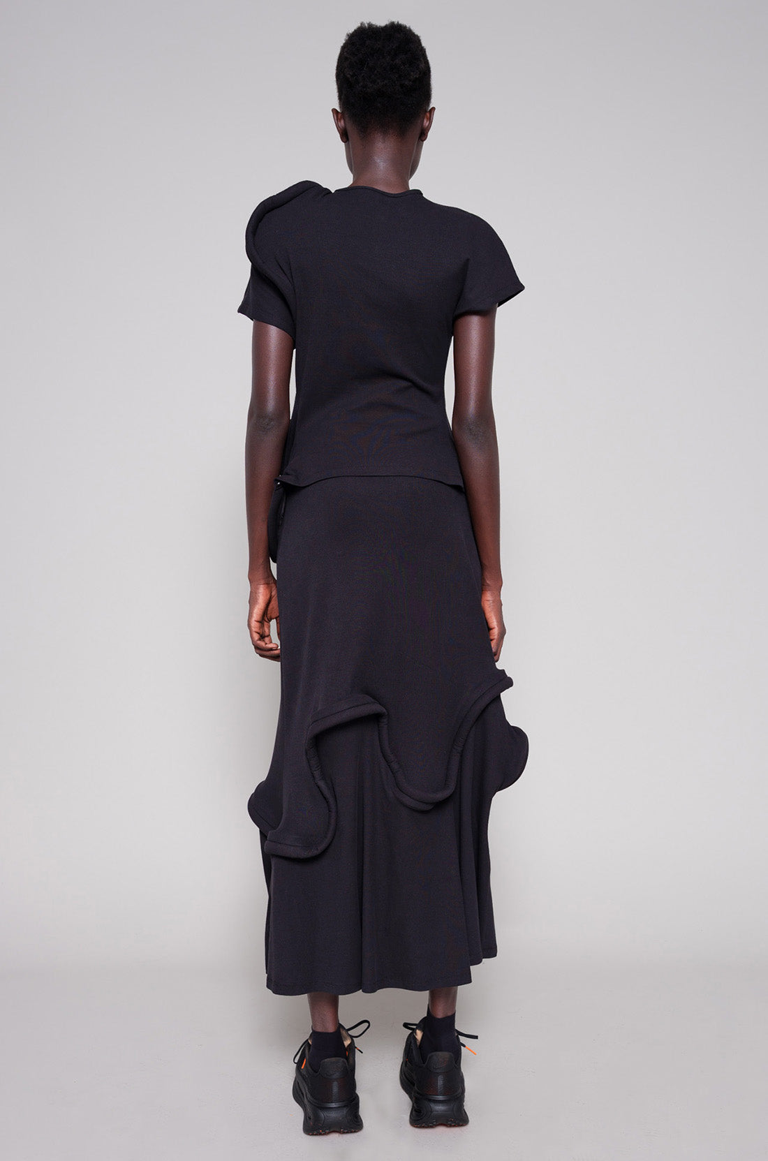 Person wearing a black top and skirt with swirl details against a plain background