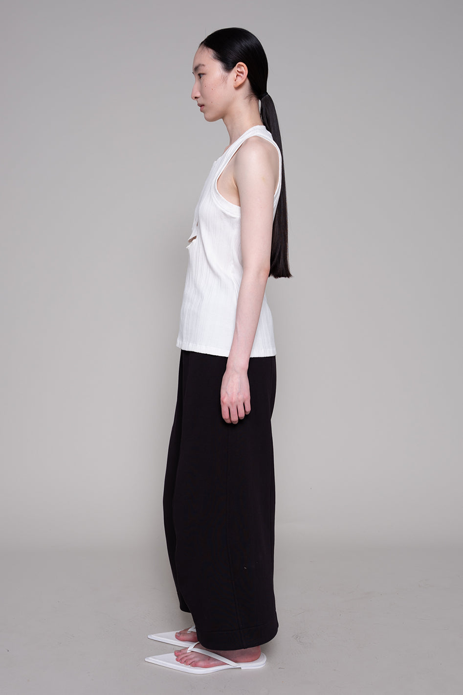 Woman wearing a white sleeveless top and black pants on a gray background