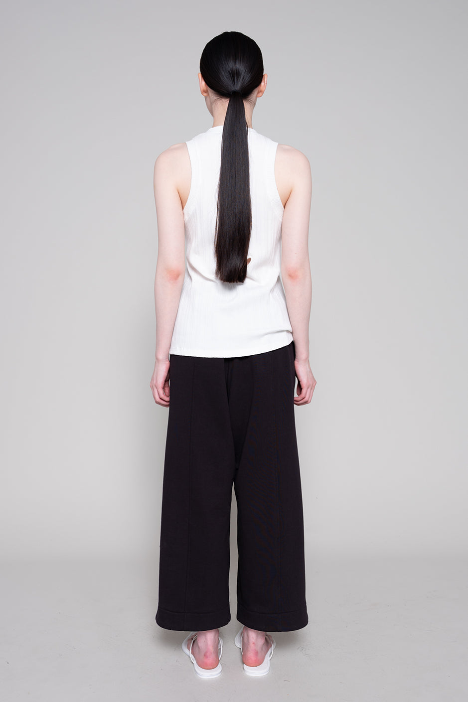 Person wearing a white sleeveless top and black wide-leg pants on a gray background