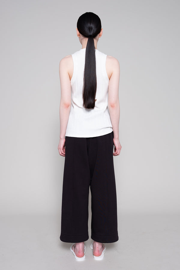 Person wearing a white sleeveless top and black wide-leg pants on a gray background