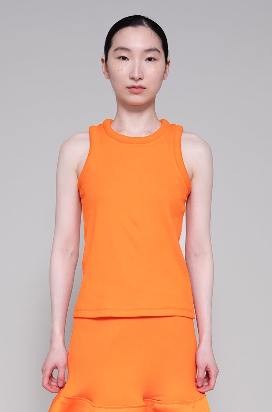 Person wearing sleeveless orange top and skirt on plain background