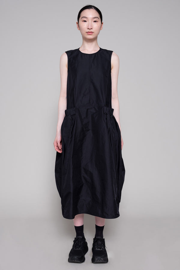 Person wearing a black sleeveless dress and sneakers against a plain background