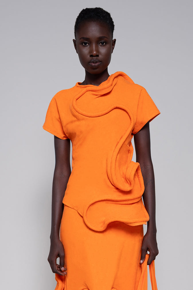 Model on a grey background wearing an orange top with a foamy swirl throughout