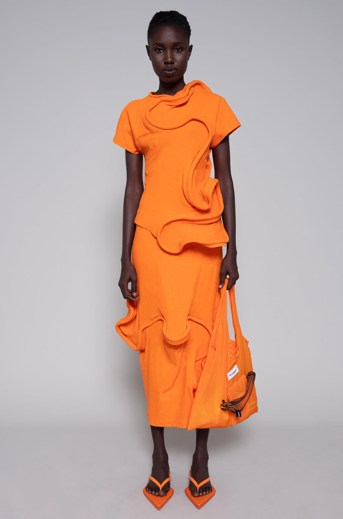 Model wearing an orange outfit with a plain background