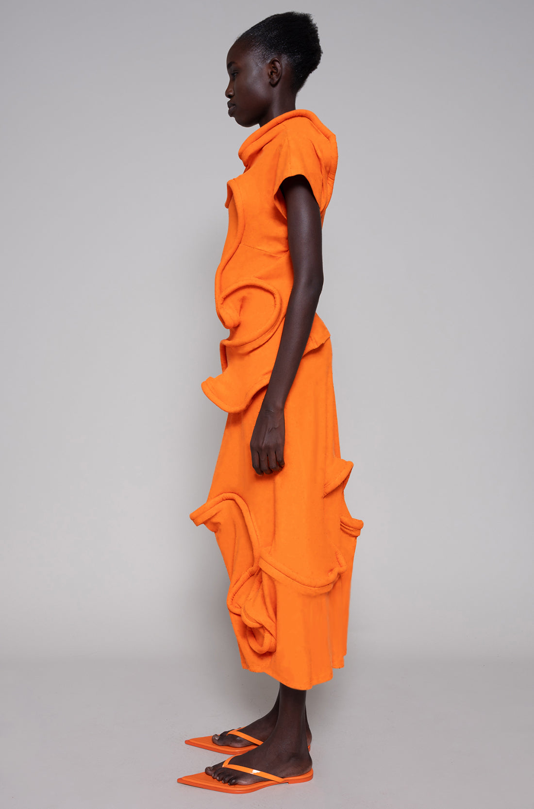 Person wearing an orange skirt and top standing against a gray background