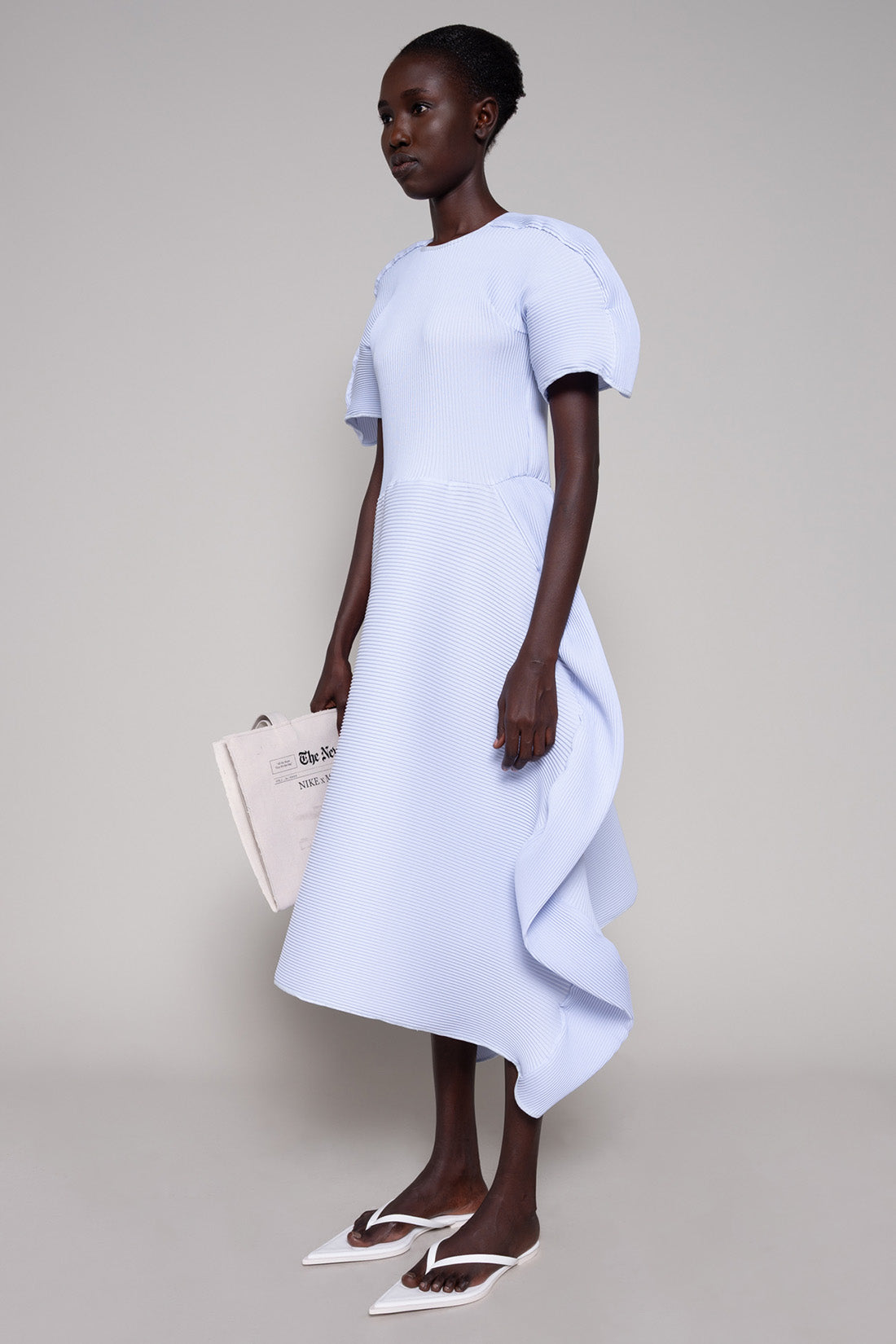 Person wearing a light blue dress holding a tote bag  against a plain background