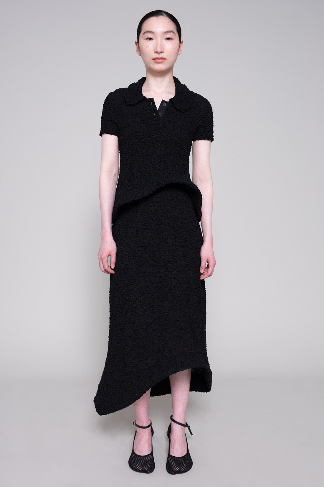 Person wearing textured matching top and skirt with heels on plain background