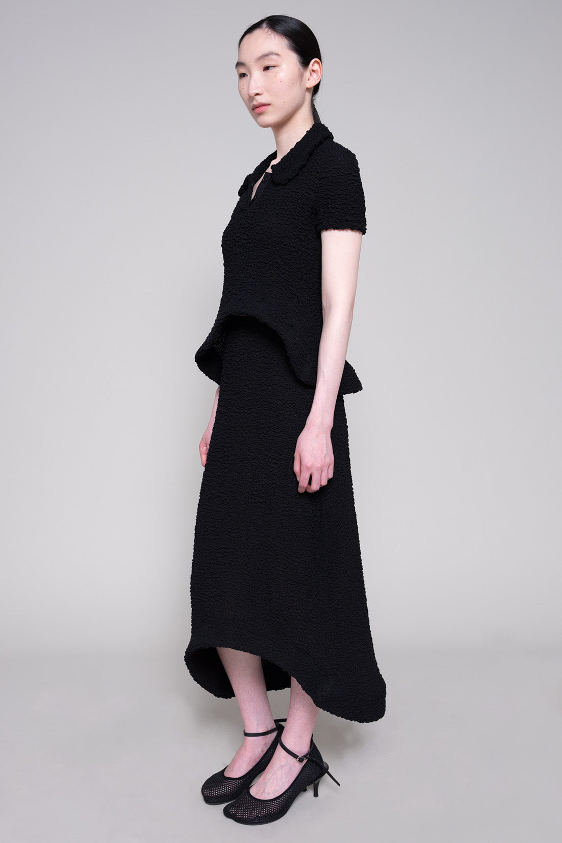 Person wearing textured matching top and skirt with heels on plain background