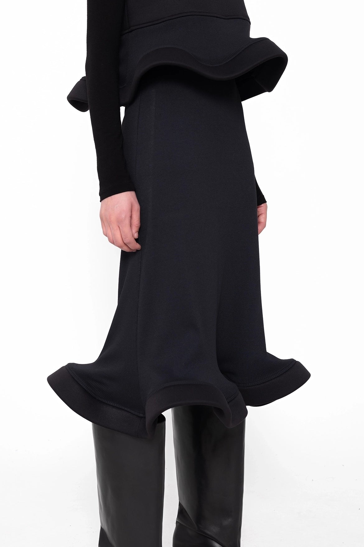 female-wearing-black-sleeveless-tp-with-wavy-hem-and-midi-black-skirt-with-wavy-hem-on-white-background-skirt-closeup-three-quarter