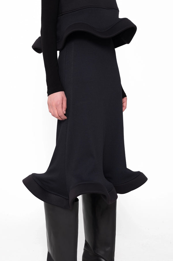 female-wearing-black-sleeveless-tp-with-wavy-hem-and-midi-black-skirt-with-wavy-hem-on-white-background-skirt-closeup-three-quarter