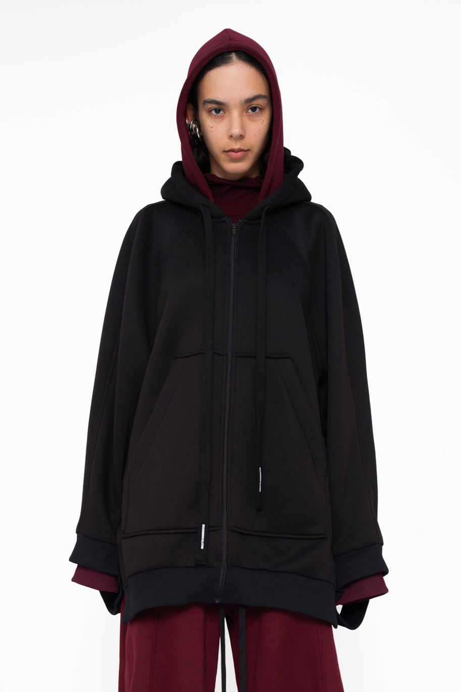 female-wearing-black-oversized-zip-up-hoodie-with-double-hood-in-black-and-bordeaux-on-white-background-closeup-front