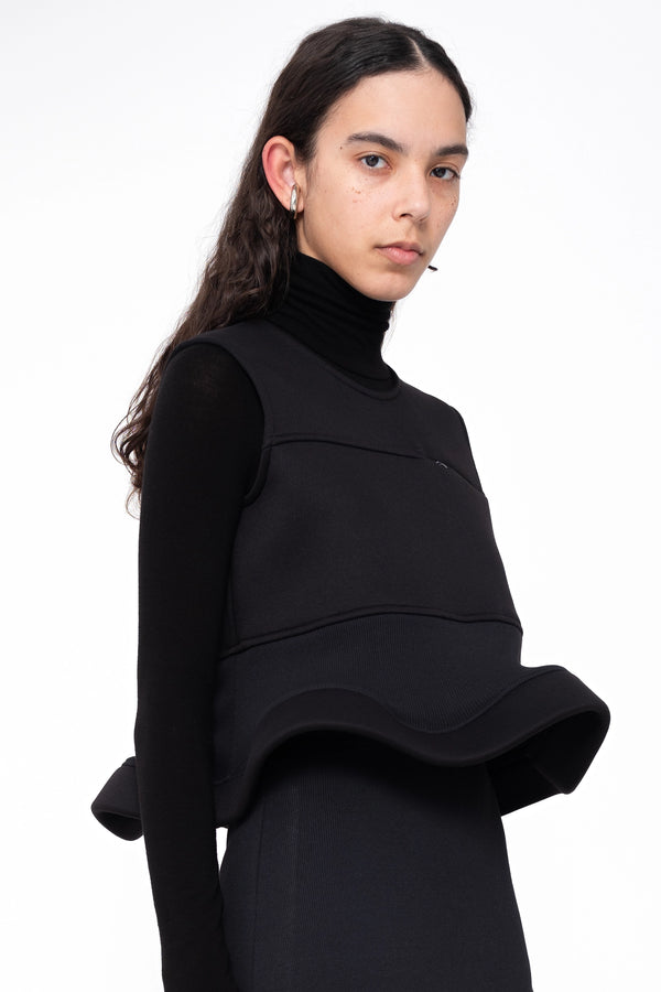 female-wearing-black-sleeveless-top-with-zip-detail-and-wavy-hem-on-white-background-close-up-torsothree-quarter